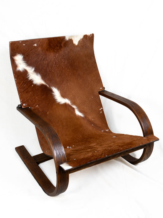 Brown and white cowhide lounge chair with sweeping dark wood arms and curved supports.